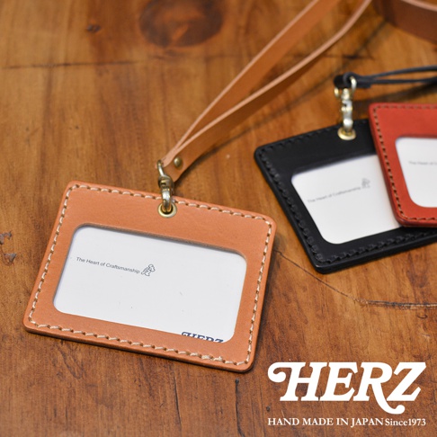 職人手作皮革橫式證件識別夾，展示了淺棕色、黑色和紅色三種顏色。淺棕色證件夾有著精緻的縫線和皮革吊繩，中間有透明視窗，印有「The Heart of Craftsmanship」字樣。