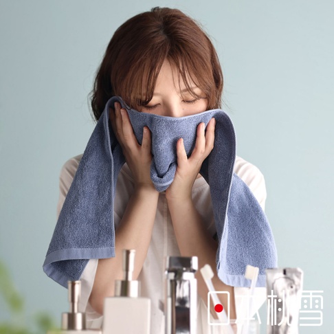 一位女子正用一條藍色毛巾擦拭臉部，周圍擺放著幾瓶盥洗用品。