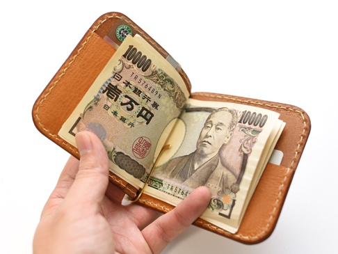 職人手作淺棕色皮革橫式對折兩用收納短夾，夾有日圓鈔票，內含卡槽，邊緣縫線清晰。