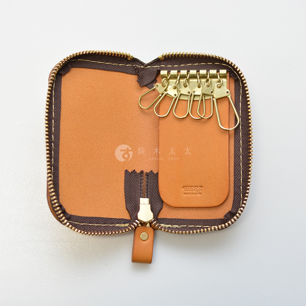 職人手作皮革橢圓形拉鍊鑰匙包，內有六個金色掛鉤，棕色皮革內裡，拉鍊為金色，附有皮革拉環。