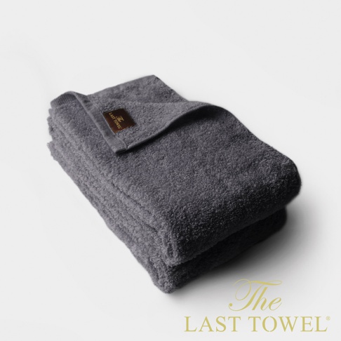 一組兩條深灰色純棉長毛巾，質地柔軟，一條毛巾上帶有品牌標誌的咖啡色標籤。