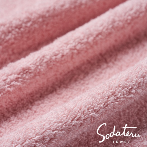 粉色毛巾的紋理特寫，展現其蓬鬆柔軟的質地，毛圈細緻，光線投射下呈現層次感。