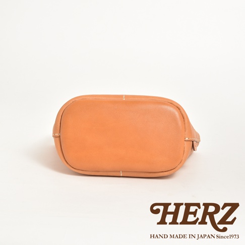 一個棕褐色皮革製成的手提午餐袋，底部呈現圓潤的弧度，並有明顯的縫線裝飾。