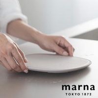 marna TOKYO 1872 品牌淺色圓盤，由雙手輕輕扶著