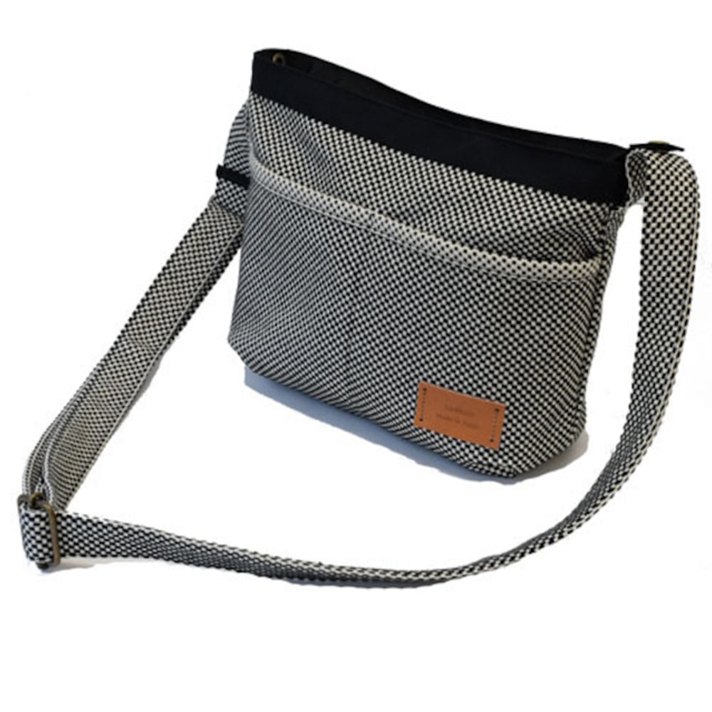 三河木綿刺子織斜背包，黑白格紋織紋，搭配黑色邊緣與織帶，附有棕色皮革品牌標籤。