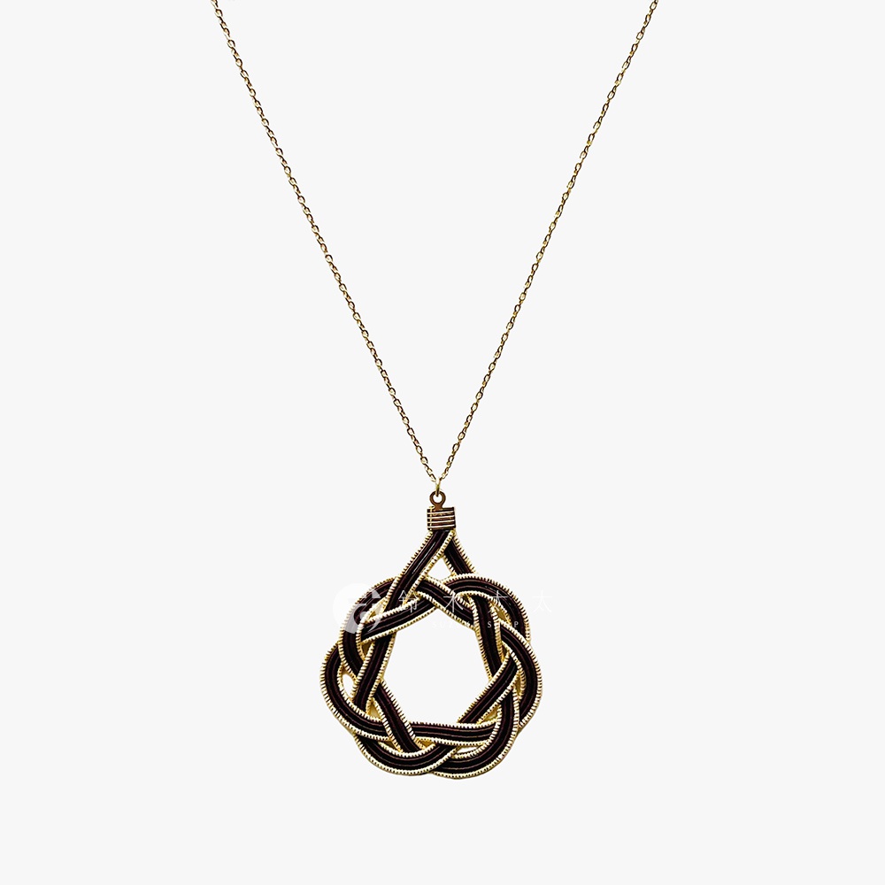 一條細長的金色項鍊，墜飾為一個以深色線材編織而成的幾何花結，金絲纏繞其中，整體呈現精緻的日式和風美學。