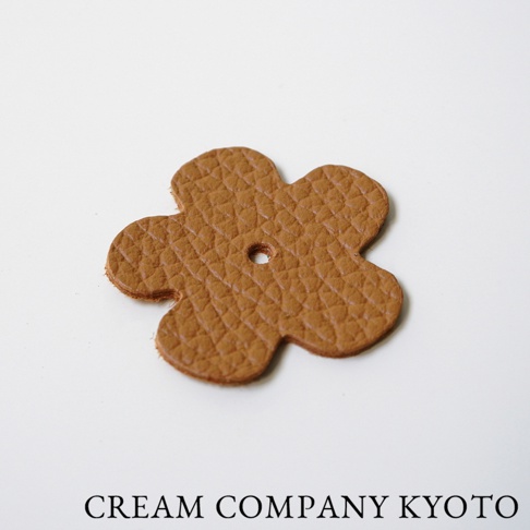 淺棕色皮革製成的五瓣花形吊飾，表面有菱格紋壓紋，中央有一小圓孔。