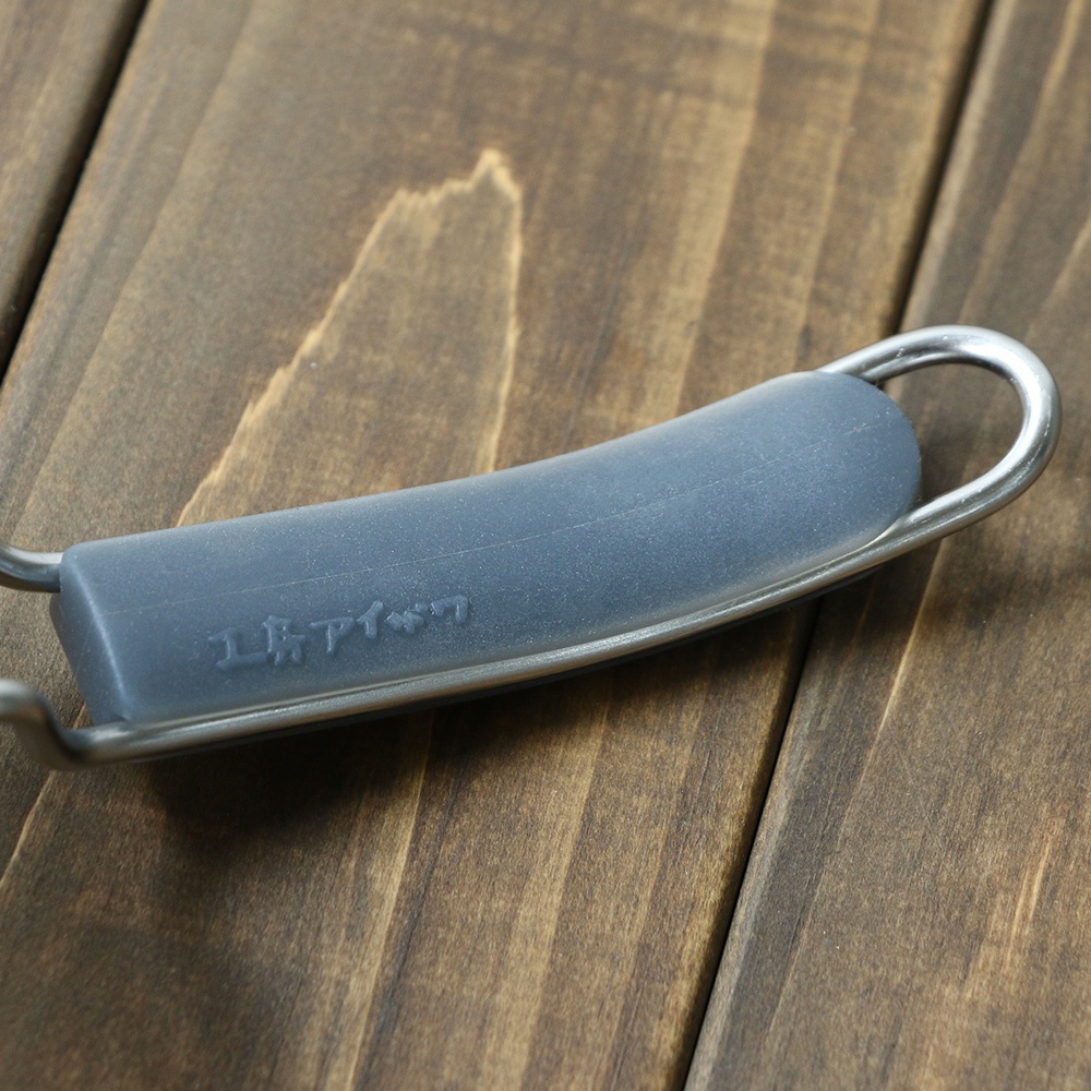 不鏽鋼濾網握柄特寫，握柄部分為灰色矽膠材質，印有日文壓紋，整體置於木質桌面。