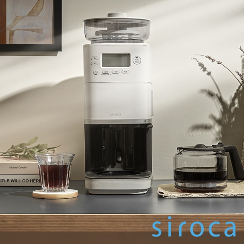 SC-C2510 石臼式全自動研磨咖啡機，淺灰色機身，配有透明咖啡豆槽、數位顯示面板和操作按鈕。機身下方為黑色咖啡滴漏區，旁邊擺放著裝有咖啡的玻璃壺和玻璃杯。