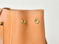 淺棕色皮革托特包，頂部有精細的縫線裝飾，兩側各有一個金色金屬原子釦，展示皮革紋理與質感。