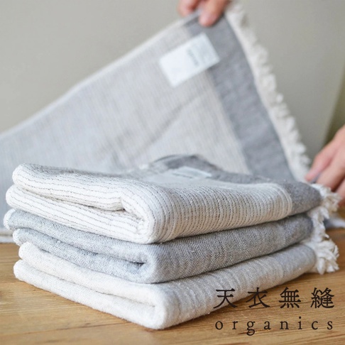 堆疊四條 HEATHER 有機混紡棉浴巾，呈現不同深淺的灰色和白色條紋，織物質感明顯，邊緣飾有流蘇。