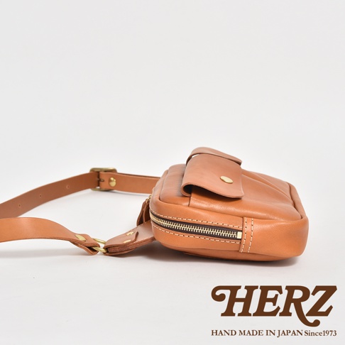 職人手作皮革雙口袋斜背包，採用棕色皮革製成，設有拉鍊主袋和翻蓋前袋，搭配金屬扣具的皮質揹帶。