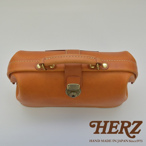 職人手作皮革長型迷你醫生包，呈現溫潤的淺棕色調，使用厚實的皮革材質，搭配復古金屬鎖扣與銅色五金配件，質感細緻。