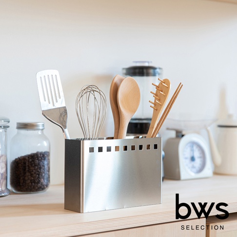 不鏽鋼餐具收納架，側面有方形孔洞，收納著不鏽鋼鍋鏟、打蛋器、木勺和筷子。
