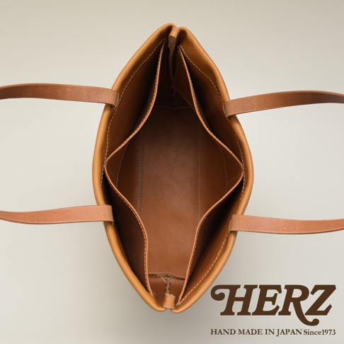 職人手作皮革托特包，淺棕色，內部有四個隔層，頂部有兩條皮革提把，以俯視角度拍攝。