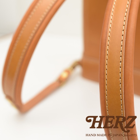 職人手作皮革立體商務後背包，特寫皮革肩帶的細緻縫線與雙色皮革拼接，展現經典焦糖棕色調，與部分背包主體。