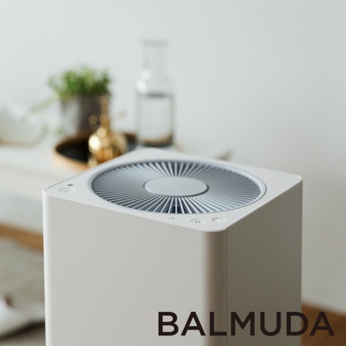 The Pure 空氣清淨機，白色方形機身，頂部設有灰色圓形風扇網罩，網罩中央有品牌標誌。機身側面可見控制按鈕，背景為模糊的室內裝飾。