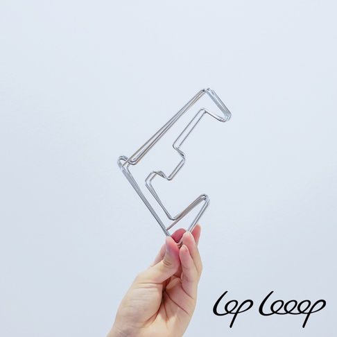 一隻手拿著一個銀色金屬製的伸縮式砧板架，其設計呈階梯狀，材質為不鏽鋼，背景為淺灰色。