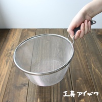 一只手正握著一個直徑約20公分的銀色不鏽鋼濾網，濾網網眼細密，邊緣有加固。濾網的握柄部分為黑色矽膠材質，末端有掛孔。