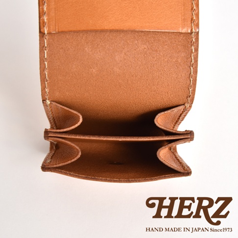 這是一張日本HERZ職人手作皮革零錢包的內部特寫照片，呈現淺棕色皮革材質與細緻的縫線工藝，展示了具有雙層收納結構的開口設計，下方印有HERZ品牌標誌與手工製造資訊。