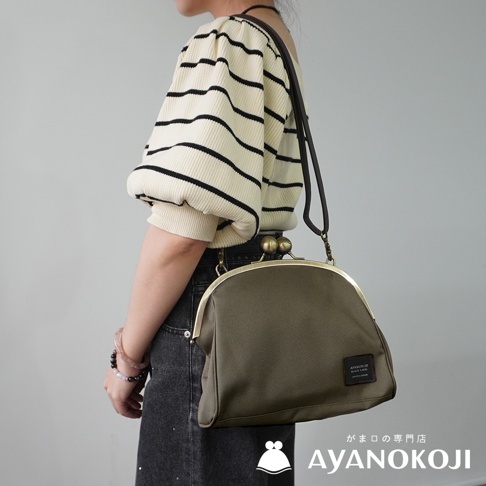 一位女性身穿條紋上衣和牛仔褲，斜挎一個深綠色的 AYANOKOJI 口金斜背包。