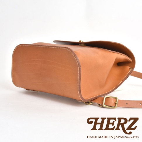 職人手作皮革翻蓋迷你後背包 R-34，採用天然棕色皮革製成，整體呈現圓潤飽滿的設計，搭配金屬扣環與細緻車縫線，質感優良。