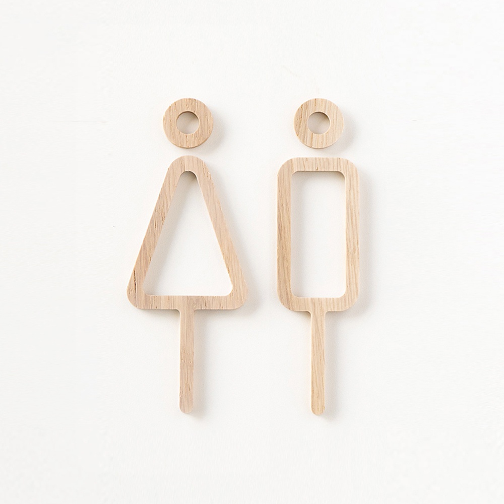 一對鏤空設計的木製男女廁所標示牌，左側為三角形代表女性，右側為長方形代表男性，均以天然木質製成，呈現簡約風格。