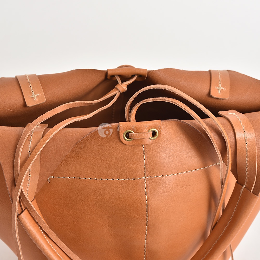 職人手作皮革球形肩掛托特包 Q-3，特寫展示包款棕褐色皮革材質，簡約縫線設計，附有可調節的皮革提把與束繩開口，細節處可見金屬孔眼。