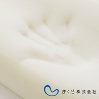 米白色記憶棉半身枕，表面有明顯的壓痕，質地柔軟。右下角有藍色曲線標誌及日文「まくら株式会社」字樣。