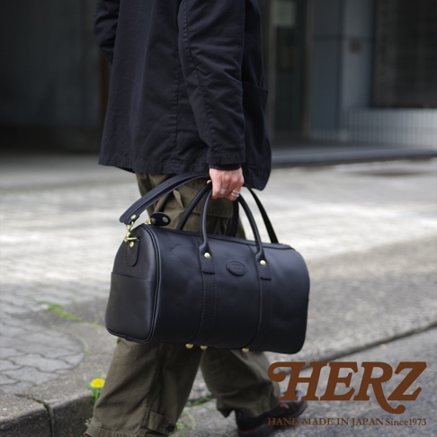 職人手作黑色皮革波士頓包，圓筒狀設計，配有雙提把及可拆卸肩背帶，金色五金配件，質感厚實。