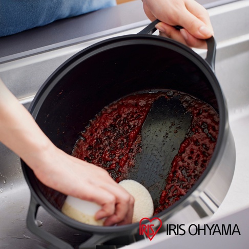 IRIS OHYAMA 萬用無水調理鍋內有殘留番茄醬，一隻手拿著鍋子，另一隻手正用海綿擦拭鍋底。