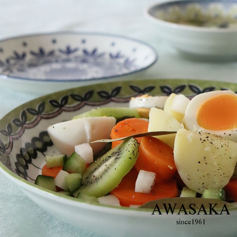 一個裝有水煮蛋、馬鈴薯、紅蘿蔔、小黃瓜塊和奇異果片的白色陶瓷料理盤，盤緣有綠色植物圖案裝飾。