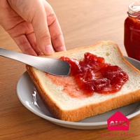 手持銀色金屬抹刀，正將紅色果醬塗抹在白吐司上，吐司和抹刀置於灰色盤子上。