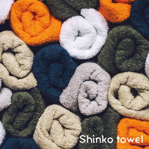 多張捲起、素面、質地柔軟的毛巾，顏色包含米白、卡其、深藍、灰、墨綠及亮橘。