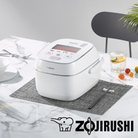 白色鐵器塗層白金厚釜壓力IH電子鍋，設有液晶顯示螢幕和多個操作按鈕，位於石紋桌面上的灰色墊子上，旁邊配有餐具、玻璃杯和水果。