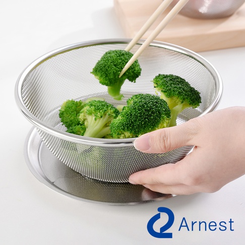 逸品物創18公分不鏽鋼瀝水籃，網狀篩網結構，裝有新鮮綠色花椰菜，由一隻手持握，背景有木製砧板。