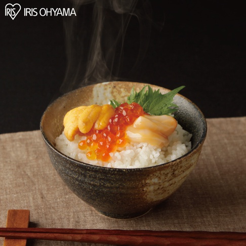 碗中盛著白米飯，飯上鋪著金黃色的海膽、鮮紅色的鮭魚卵和淡黃色的干貝。一旁點綴著綠葉，碗身為褐色漸層，背景為黑色，前方有木質筷子。