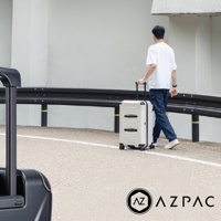 一名男子推著一個奶油色帶有黑色條紋的 AZPAC 行李箱走在路上。