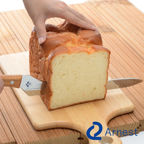 不鏽鋼麵包刀，刀刃帶鋸齒，木柄，正在切一塊金黃色外皮、內部柔軟的吐司麵包。