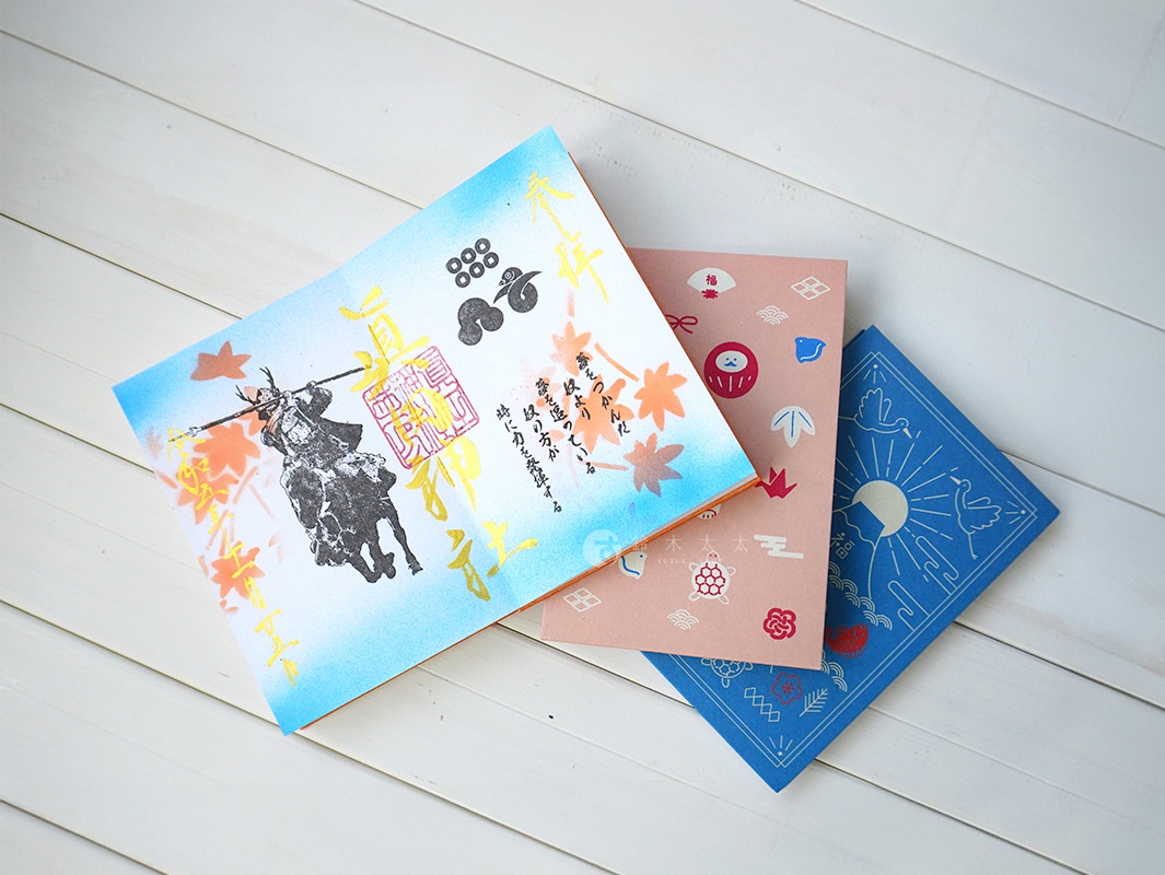 三本美濃和紙製成的御朱印帳，分別為藍色、粉色及藍白色漸層。藍白色封面印有騎馬武士、楓葉與日文文字；粉色封面印有達摩、龜、鶴等日式吉祥圖案；藍色封面則以富士山、鶴、太陽為主題。