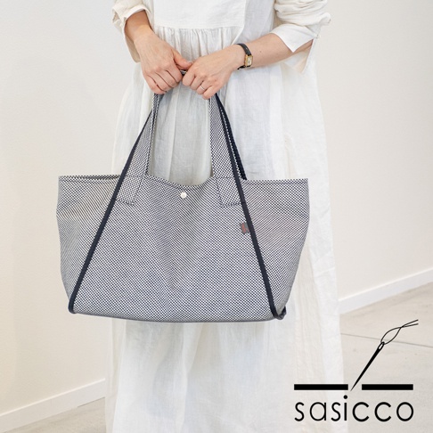 一位女士手持一個藍白格紋刺子織托特包，包邊為深藍色，有兩個肩帶，包口有一個銀色按扣。