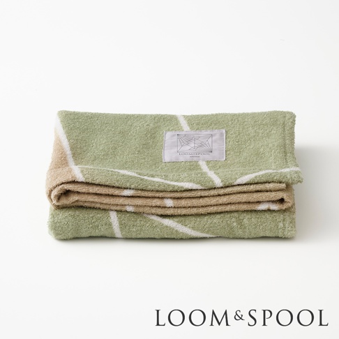 一條疊好的淺綠色純棉浴巾，帶有米色和白色的幾何線條圖案，上面有一個標籤。