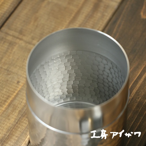 不鏽鋼錘目紋茶葉罐，銀色，帶有蜂巢狀捶打紋理，放置於木紋背景上。