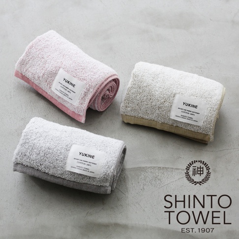 三條 YUKINE 有機棉蓬厚浴巾，分別為粉紅色、米白色與灰色，皆帶有品牌標籤，材質柔軟蓬鬆，呈現日式簡約風格。