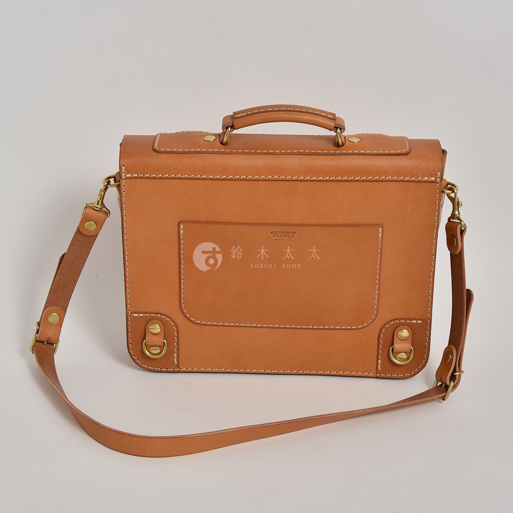 職人手作皮革歐風三用學生包，採用棕色皮革，設有提把、可拆卸側背帶及金屬扣環，正面有方形口袋，印有品牌標誌。