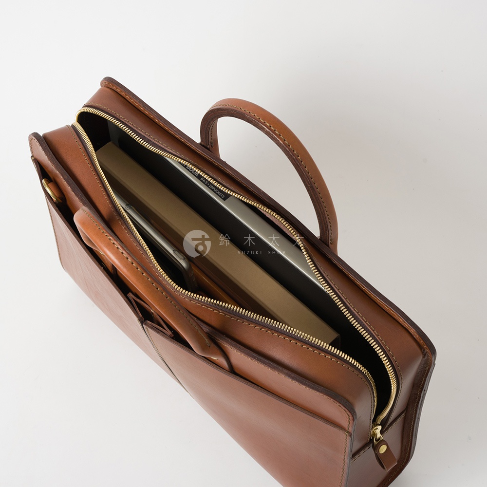 職人手作皮革雙口袋兩用商務公事包，棕色皮革材質，內有筆記型電腦和書籍，金色拉鍊，雙提把設計。