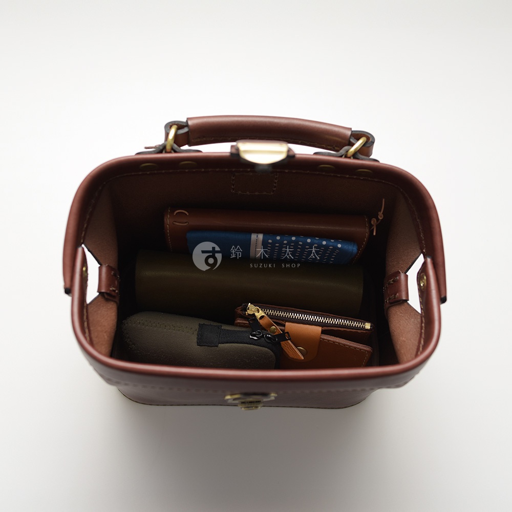 棕色皮革迷你醫生包，內部展示著錢包、筆記本、化妝包及其他小物，包款頂部配有提把與金屬鎖扣，整體為職人手作風格。