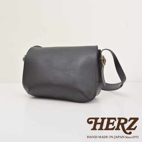 黑色皮革復古翻蓋郵差包，配有可調式肩帶和金色搭扣，展現簡約的職人手作質感。