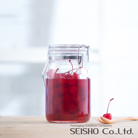 透明玻璃密封儲物瓶，裝有醃漬櫻桃，瓶蓋為金屬扣環設計。瓶旁有一支木湯匙，上面放著一顆櫻桃。
