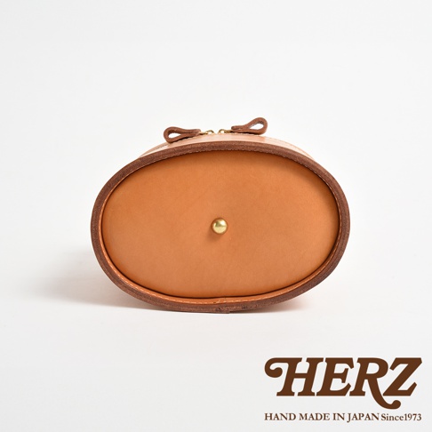 職人手作皮革圓筒型化妝手提包，淺棕色皮革，圓潤造型，頂部有金色小圓釘裝飾，兩側有皮革拉環，搭配拉鍊開合。